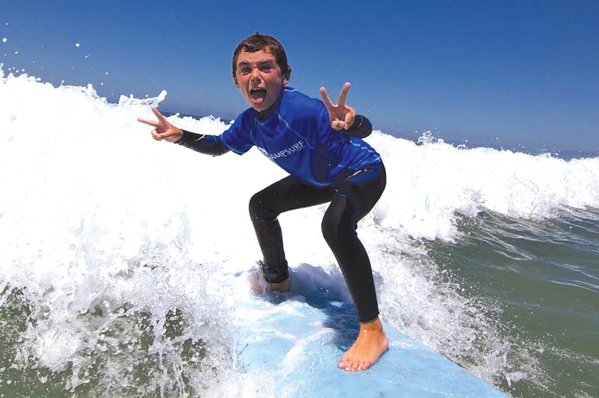 A young boy is having a fun time riding a wave at Camp Surf summer surf camp in Manhattan Beach CA