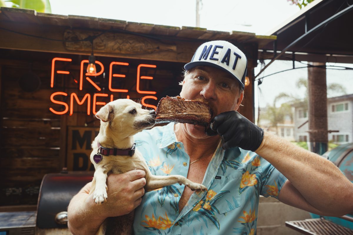 A man chews on one end of a beef rib while his pet chihuahua bites the other end.